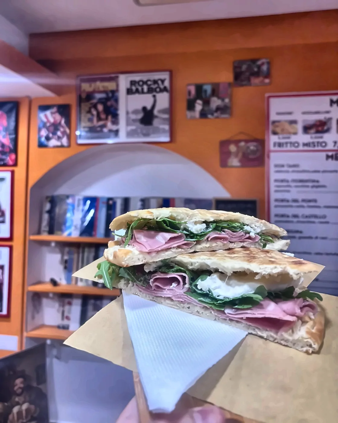 La schiacciata Luca Pacioli, con mortadella, burrata e rucola, tenuta in mano dentro Alfeo